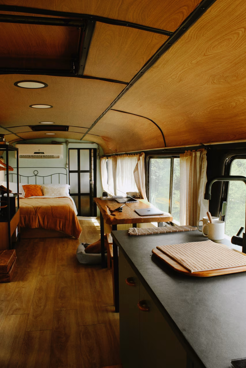Interior do Ônibus Chara com cama, mesa de madeira e cozinha